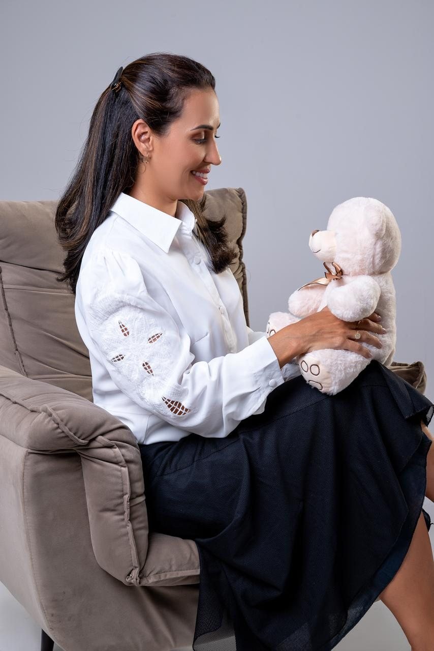 Dra. Priscilla Aquino sentada, observando com carinho um urso de pelúcia